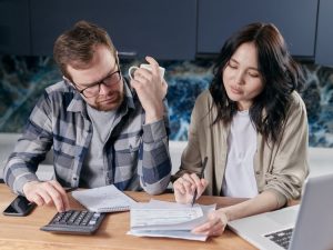 一对年轻夫妇在厨房餐桌上用计算器核对账单和收入，评估在多伦多买房需要多少收入